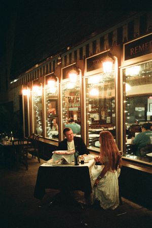Couple dining at a romantic outdoor restaurant patio at night, illuminated by warm glowing lights.
