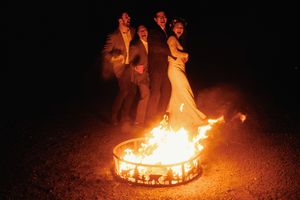 A wedding party stands dramatically near a blazing fire ring at night creating a stunning photo effect.