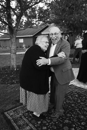 A heartwarming candid black and white photograph of two elderly people sharing a joyful laugh together outdoors.