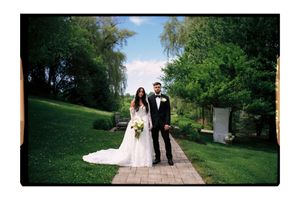 Bride and groom posing on a brick pathway surrounded by lush green trees and grass on their wedding day.