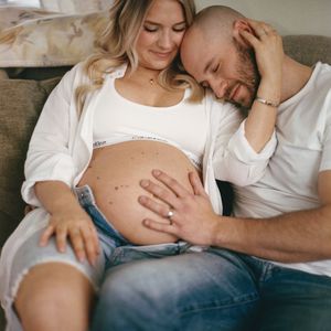 Intimate maternity photo series showing couple in casual white tops sitting together and embracing a growing baby bump.