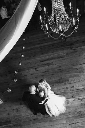 Multiple black and white photos show a figure lying alone on a wooden floor under an elegant chandelier.