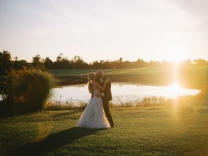 A couple shares a romantic moment on a golf course by a lake during golden hour sunset.