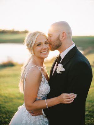 A romantic golden hour wedding photo of a couple embracing outdoors with a scenic landscape in the background.