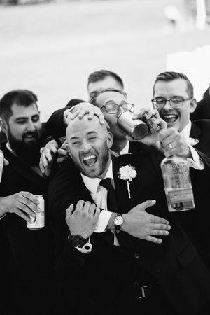 Groomsmen in black suits share laughs and drinks in a series of candid black and white wedding photos.
