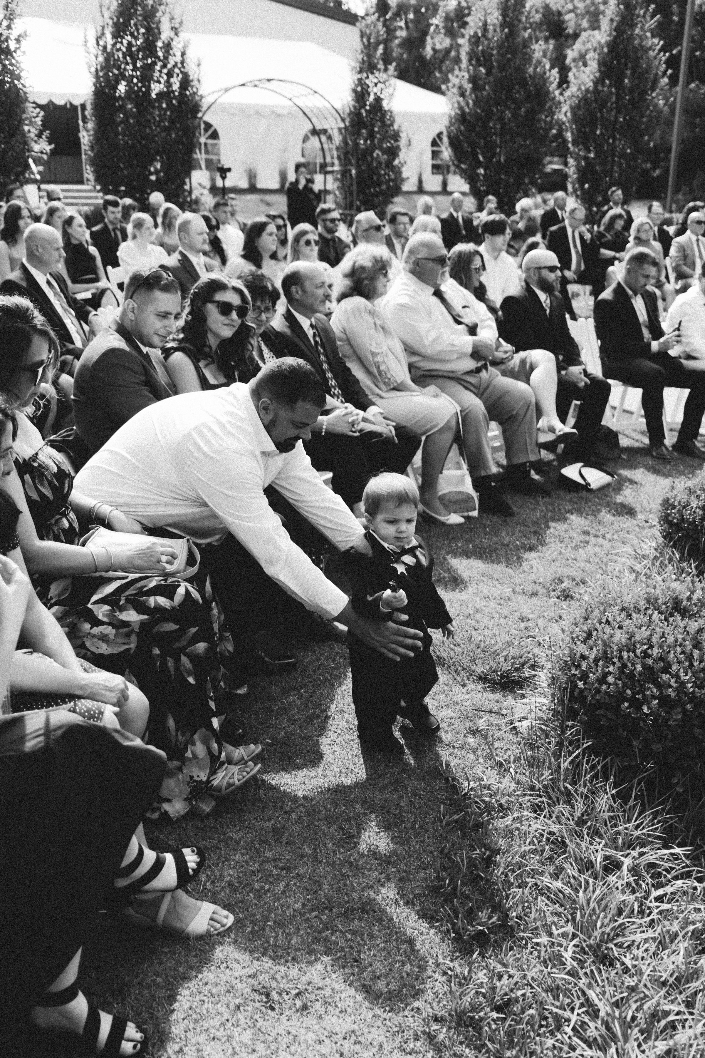 Wedding guests laugh and enjoy an outdoor ceremony in sequence of black and white candid photos.