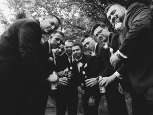 Classic black and white photo of a group of groomsmen in suits huddled together smiling at the camera.