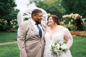 A bride and groom share a joyful moment outdoors, surrounded by lush gardens and colorful flowers on their wedding day.