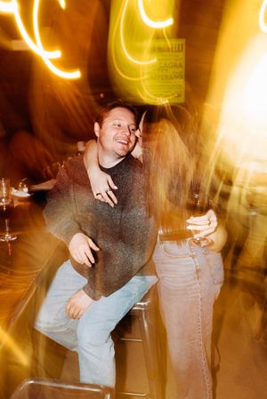 Blurred motion party photo with person dancing energetically in jeans and sweater under warm glowing lights.
