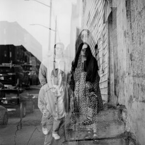 Vintage black and white double exposure photograph showing ghostly figures standing against a building wall.