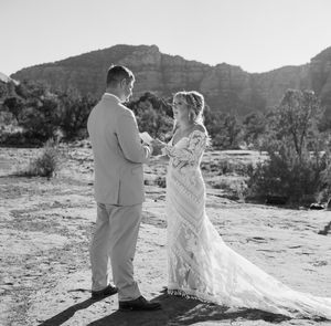 Elegant wedding couple stands together against dramatic mountain backdrop in a desert landscape in black and white.