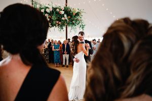 A couple shares a romantic dance during their wedding reception while guests watch from the background.