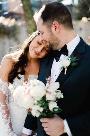 A romantic wedding moment captured outdoors with white floral bouquet and formal attire.