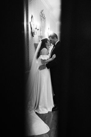 A romantic black and white wedding photo showing a couple embracing in a softly lit hallway.