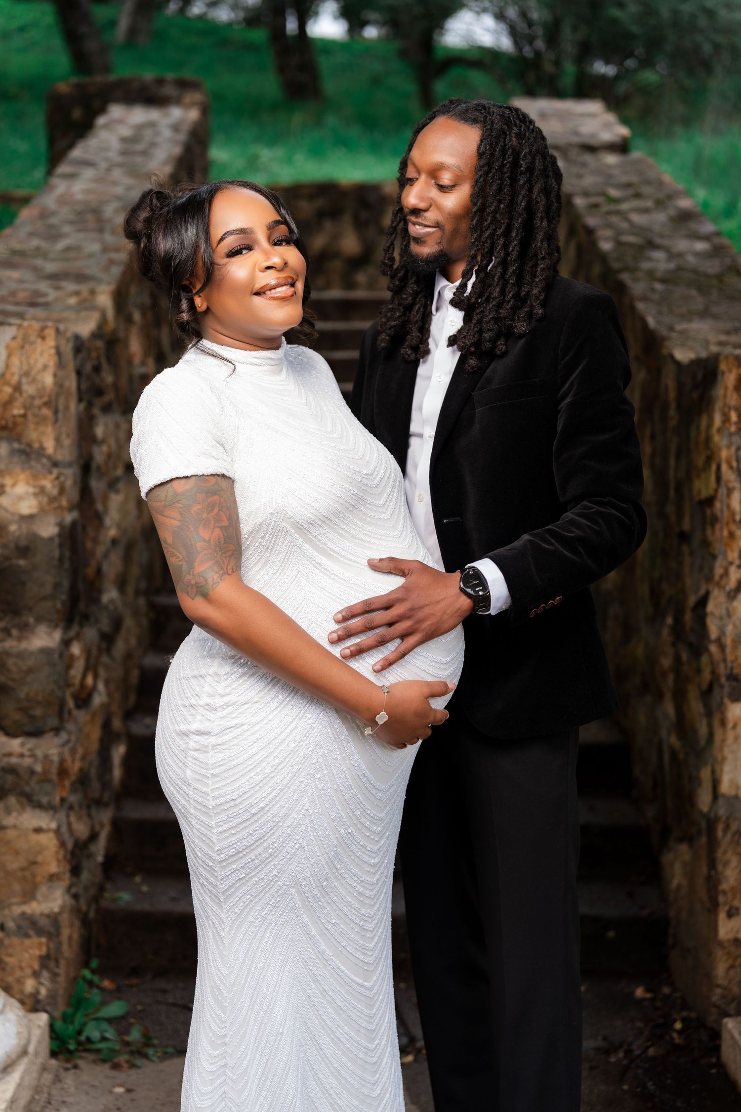 A couple in formal attire poses for a romantic maternity photo on stone steps outdoors.