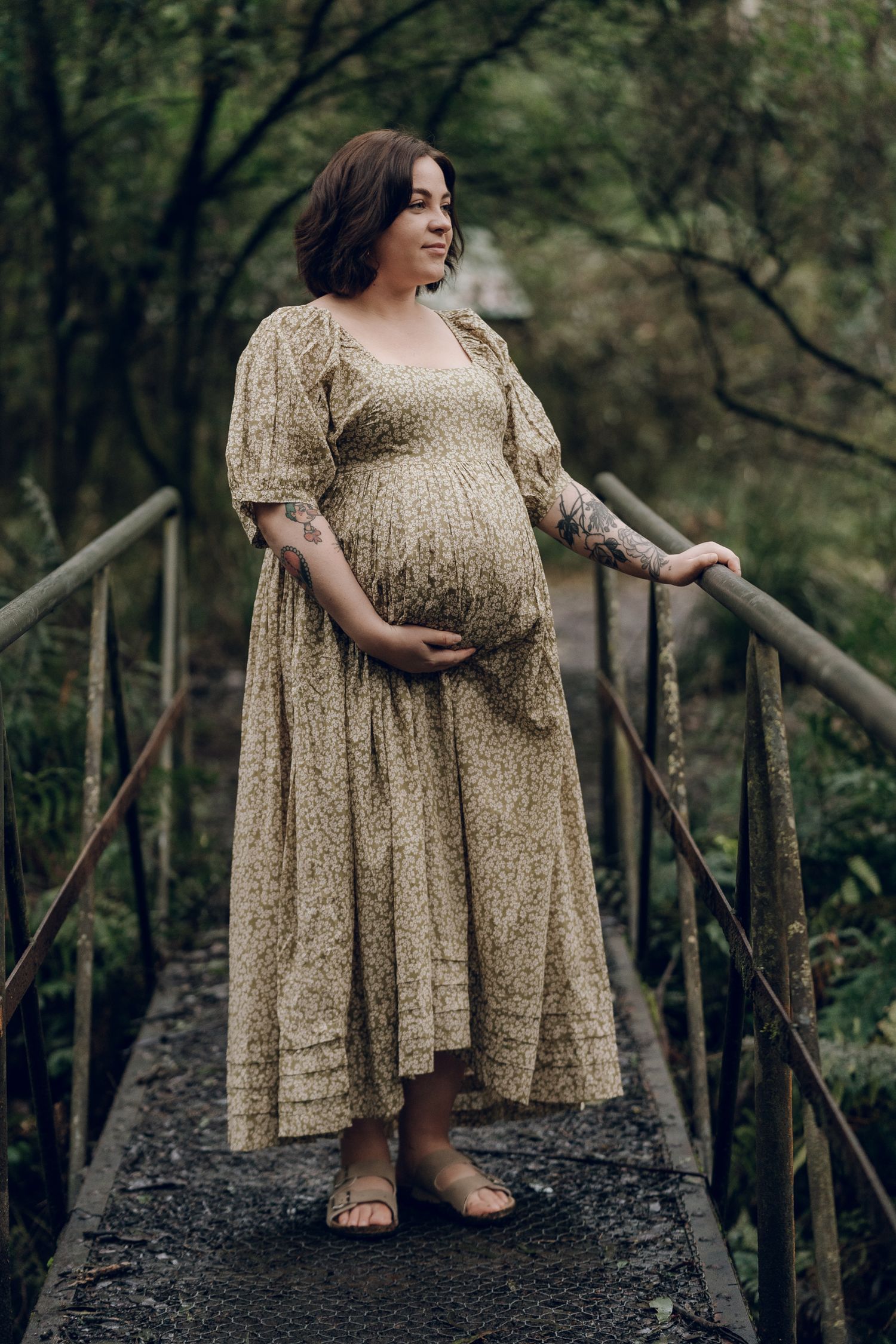 Person in flowing gold dress posing on wooden walkway in forest setting.