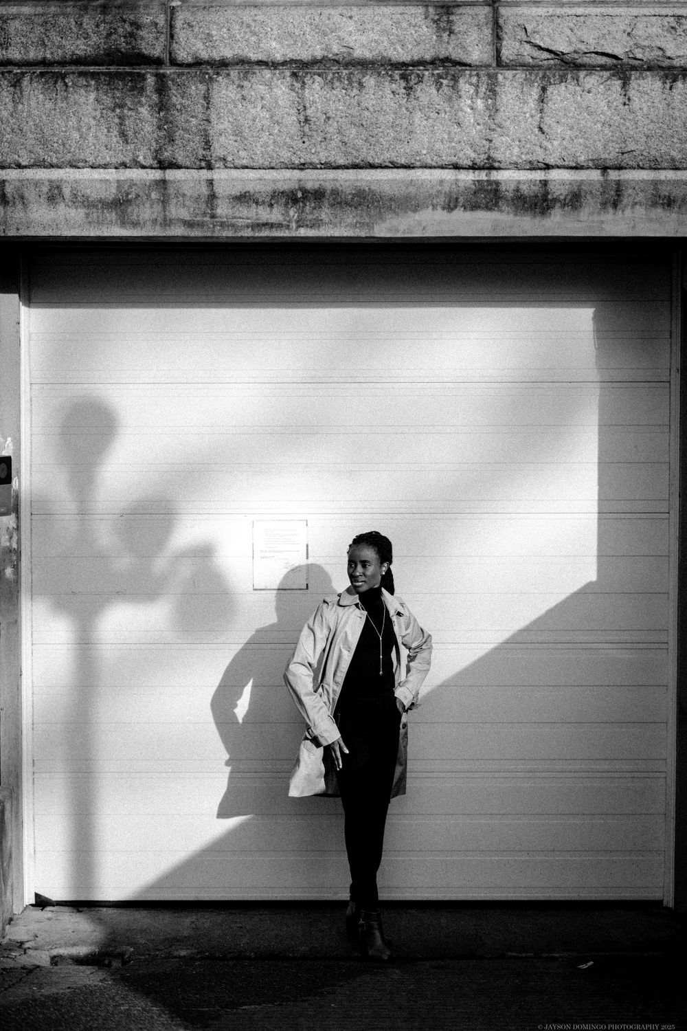 Black and white photo of person leaning against white garage door with dramatic shadow cast on wall.