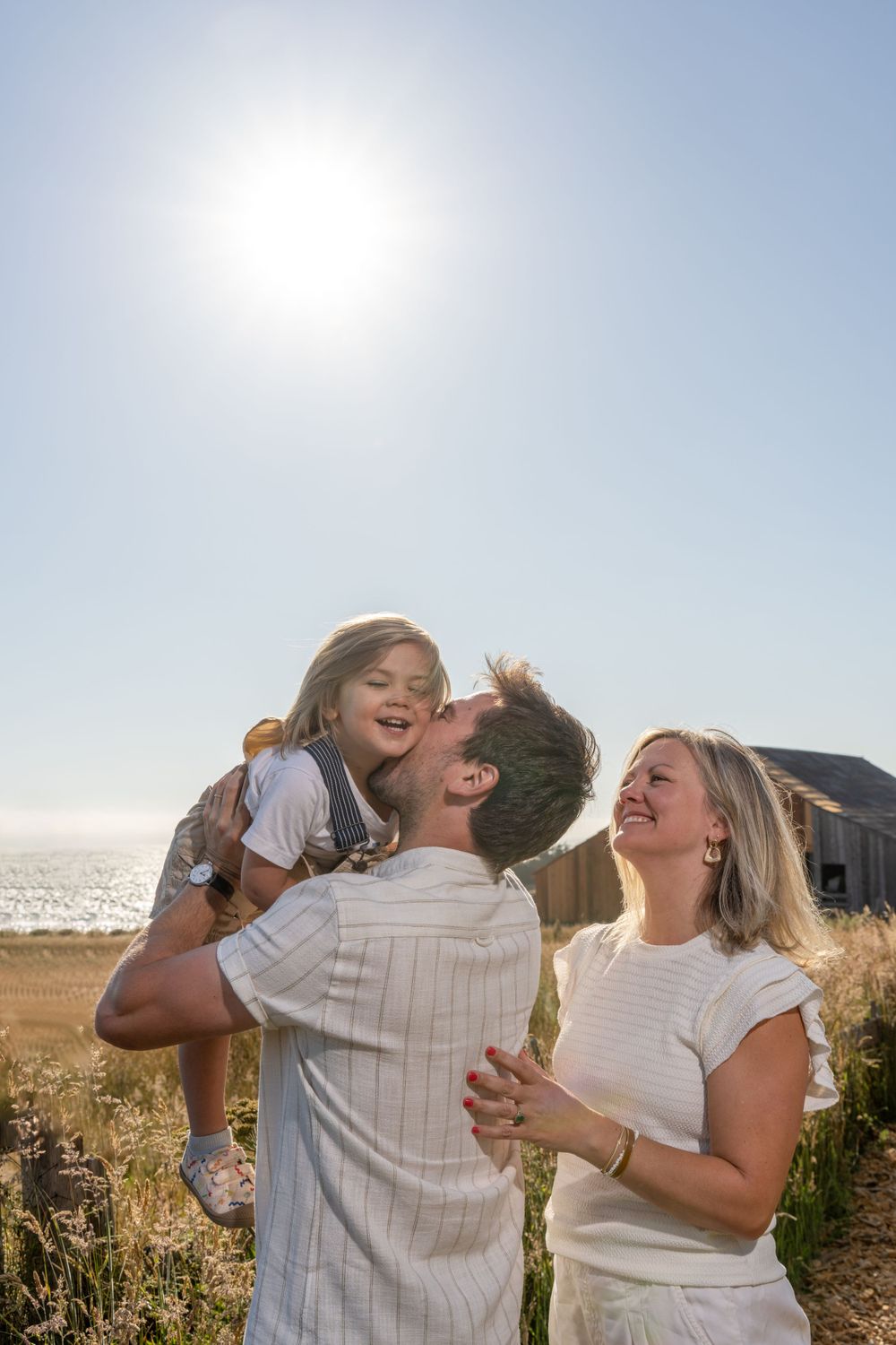 Family shares joyful laughter during sunset photoshoot by the ocean.