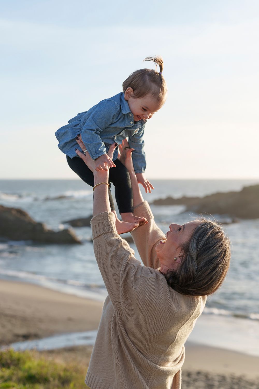 A joyful scene on a beach at sunset as someone lifts a small child playfully into the air.