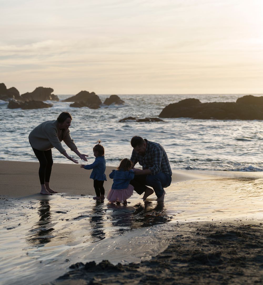 A small group explores tide pools along a rocky beach at sunset, examining marine life in the shallow waters.