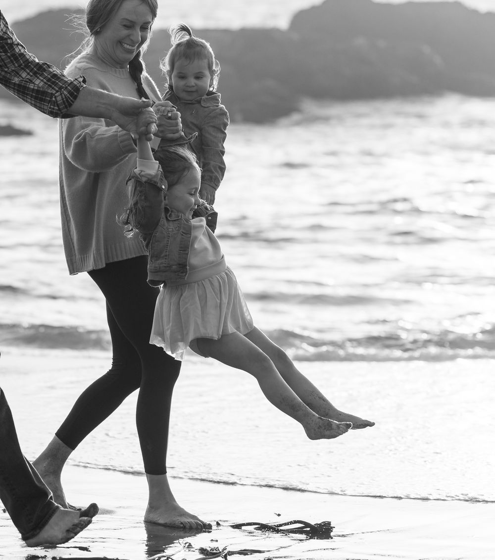 A playful beach scene with someone swinging a child by the ocean waves.
