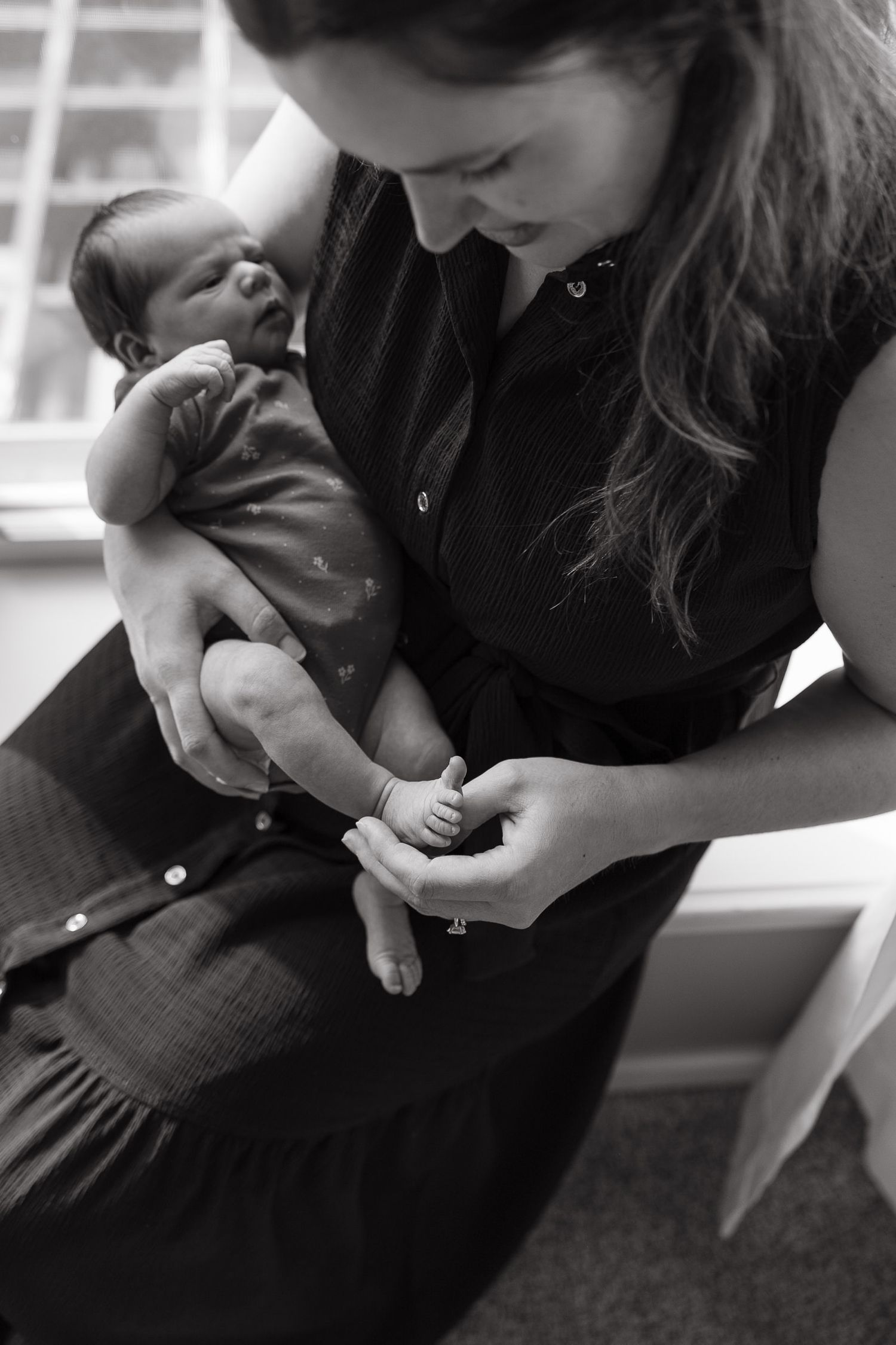 new mother counting her newborn daughters toes while sitting on a window sill