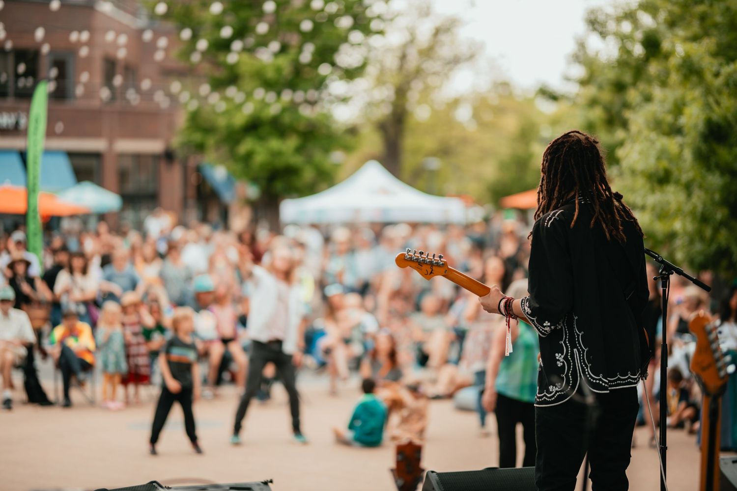 Musician performing on stage at an outdoor festival with crowd in background.
