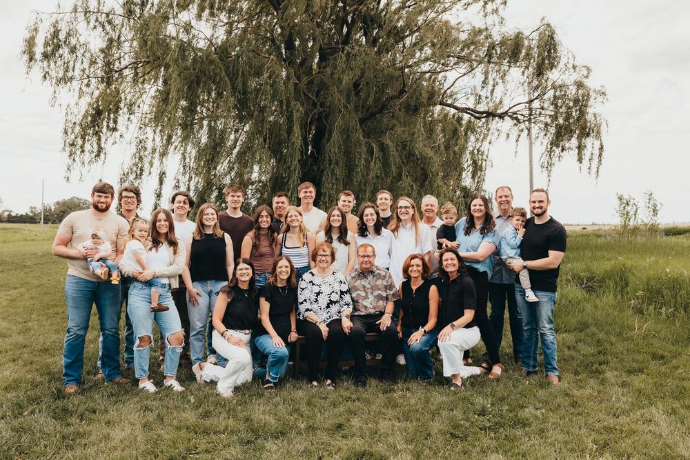 Large family group portrait outdoors under a weeping willow tree on a green lawn.
