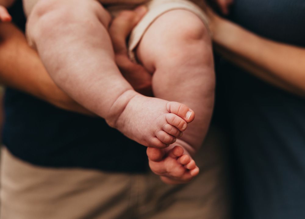 Close-up of a newborn baby's tiny feet and chubby legs being held by parents in a tender moment.