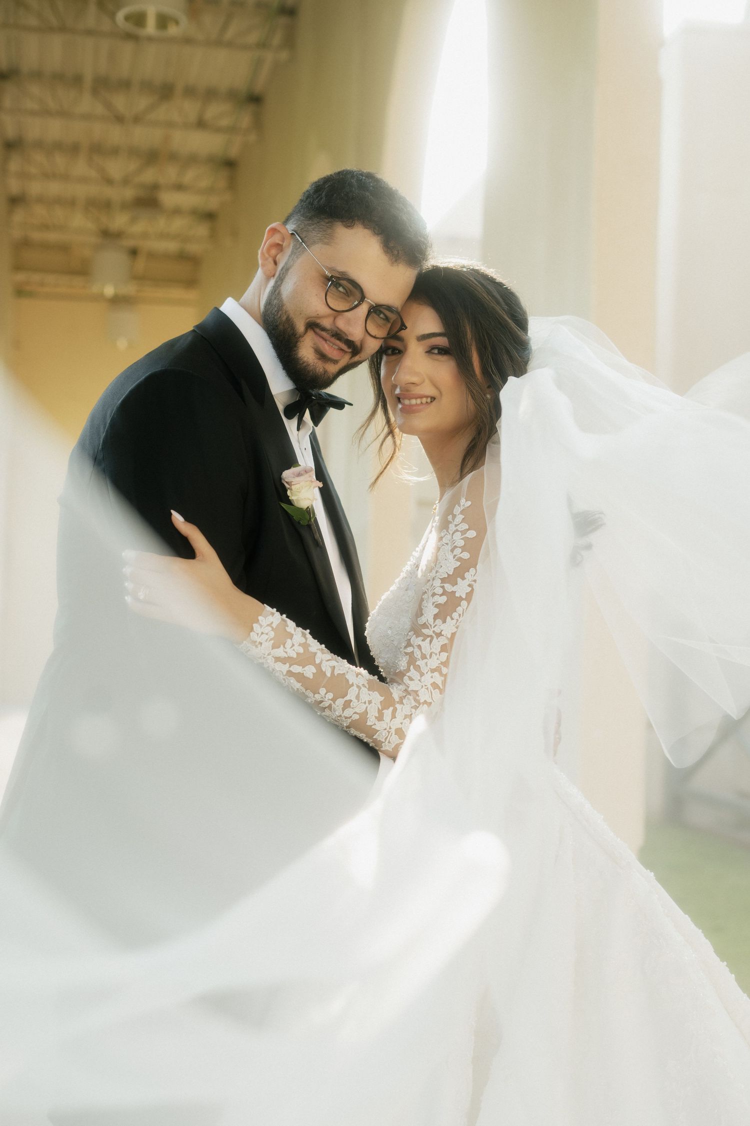 A wedding couple shares an intimate embrace while the bride's veil flows dramatically around them.