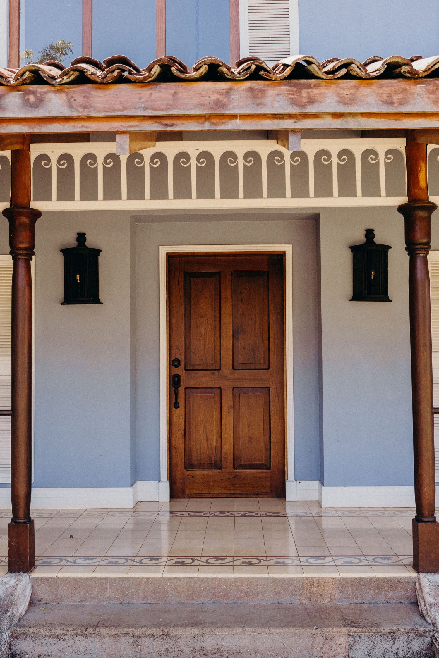 Elegant wooden front door with black wall lanterns on a blue stucco Spanish-style home exterior.