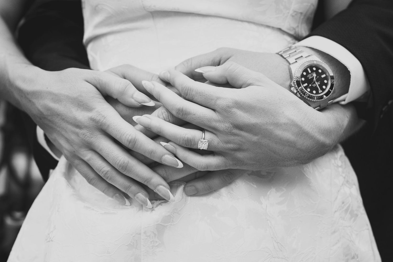 closeup of man standing behind fiancé with his arms wrapped around her waist and her hands on top of his
