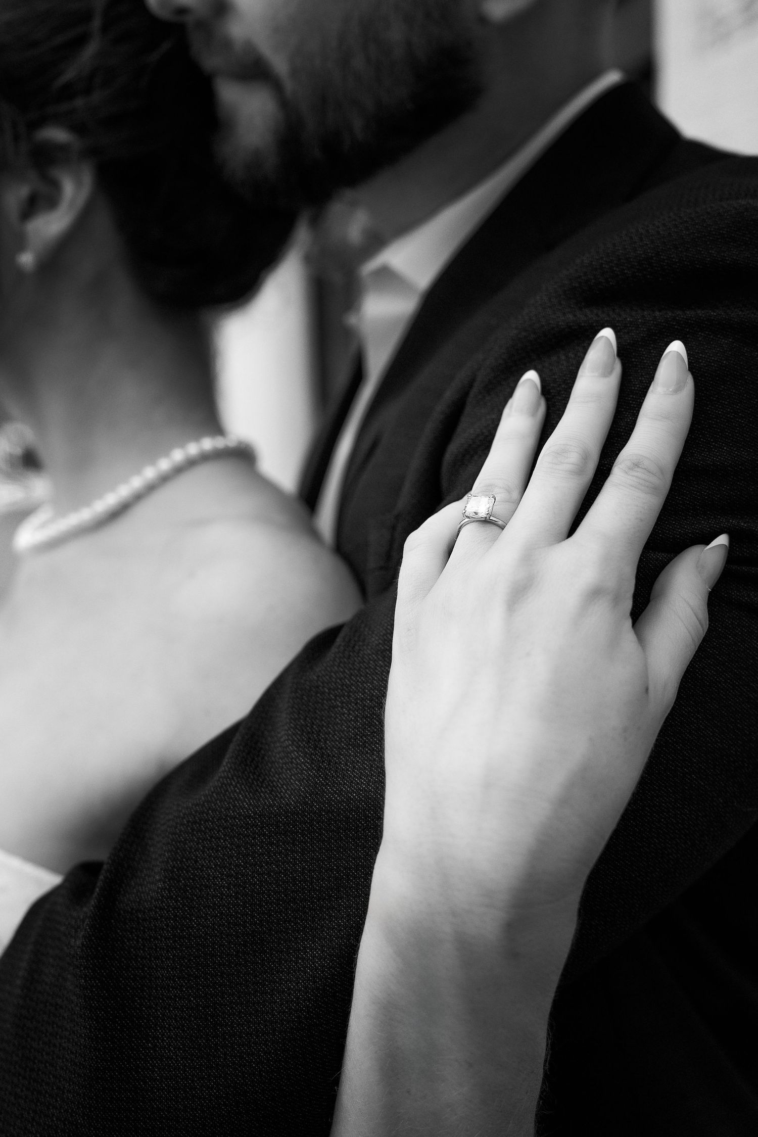 closeup of woman's hand wearing an engagement ring resting on her fiancé's shoulder