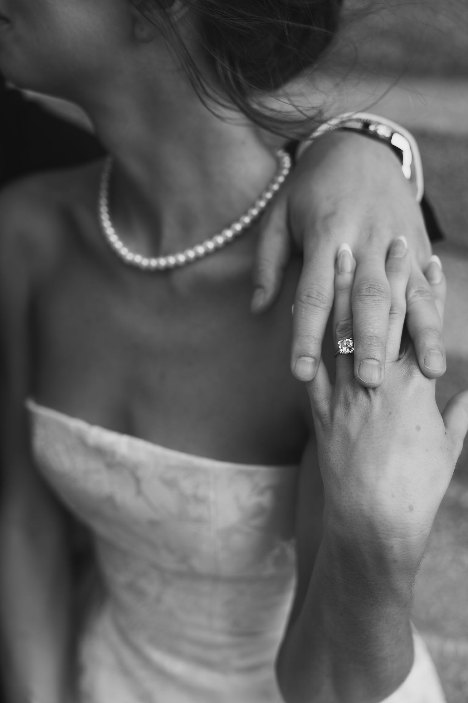 closeup of woman and man's entwined fingers and engagement ring showing through
