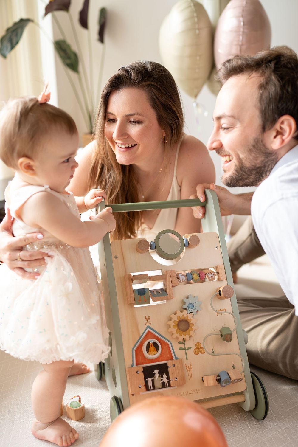 Family playing together with a wooden activity cube toy in a bright, airy room.