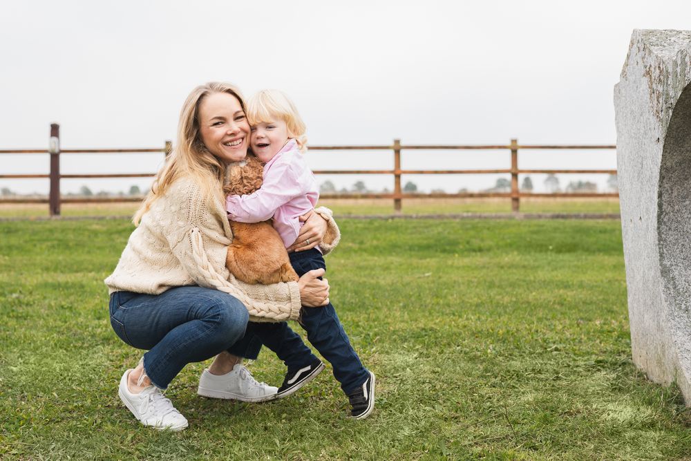 A mother and a child share a playful moment in a grassy field near a white fence in Sawston, UK