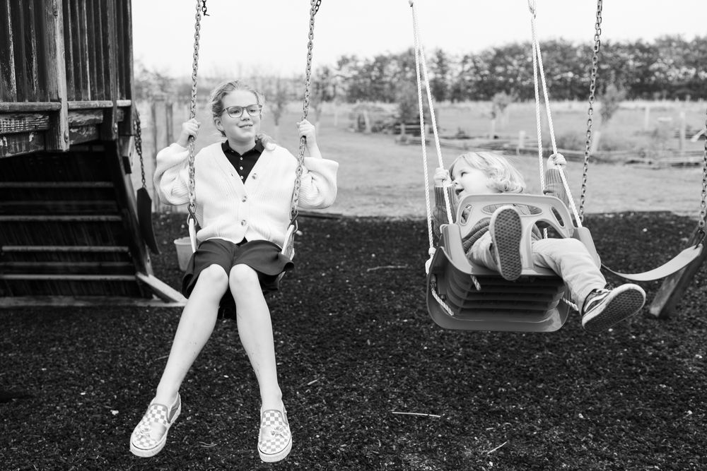 Black and white photo showing children swinging back and forth on a playground swing set.