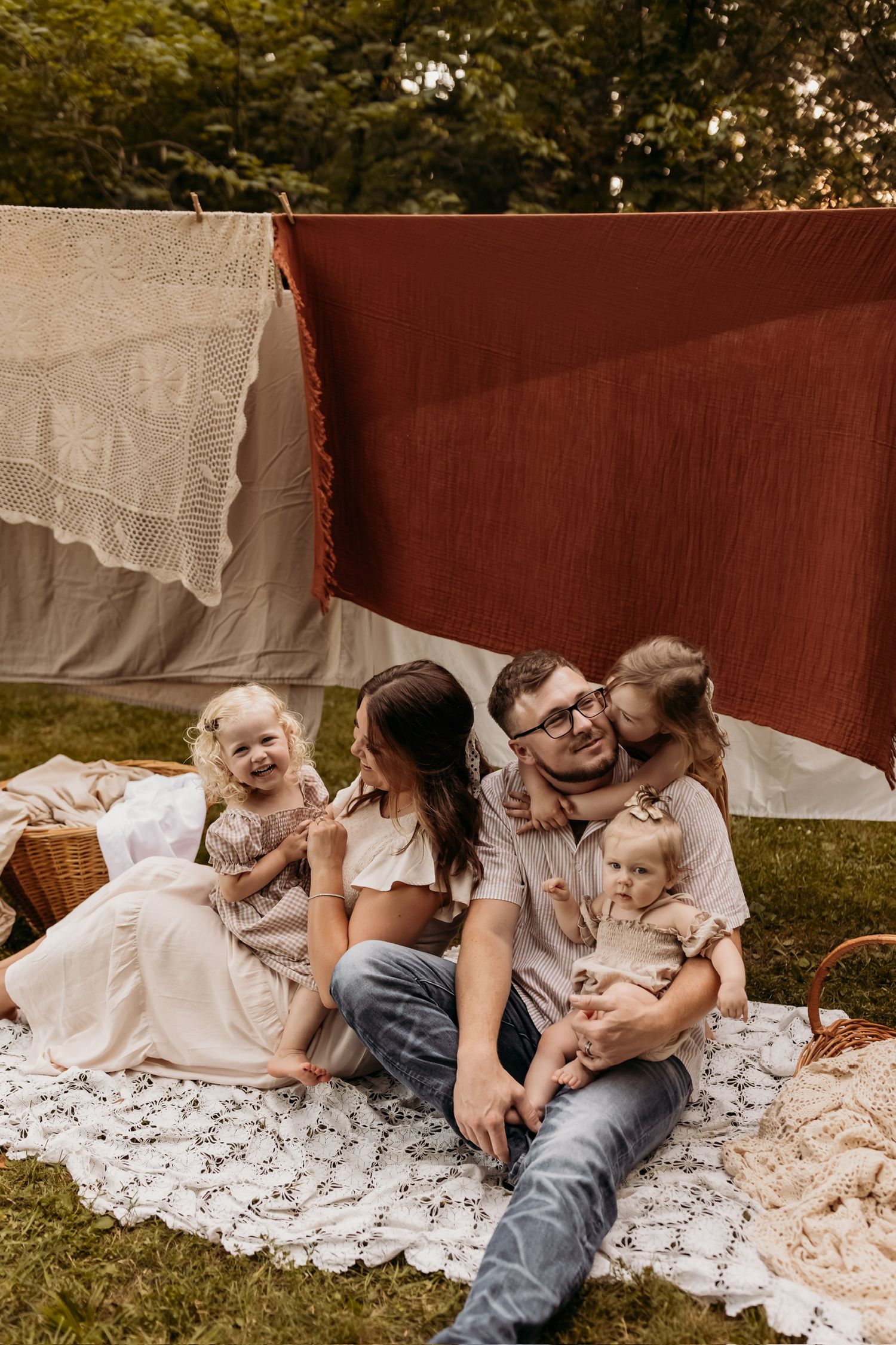 Family lounging together on white lace blanket outdoors during casual lifestyle photoshoot.