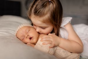 a young girl giving a newborn baby a kiss.