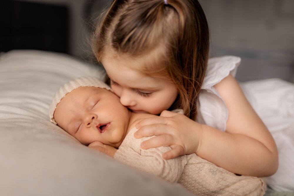 a young girl giving a newborn baby a kiss.