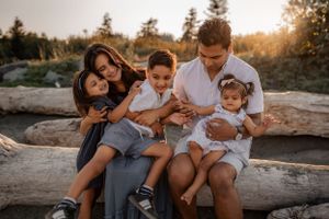 a mother, father, two young girls and a young boy, hugging on a beach.