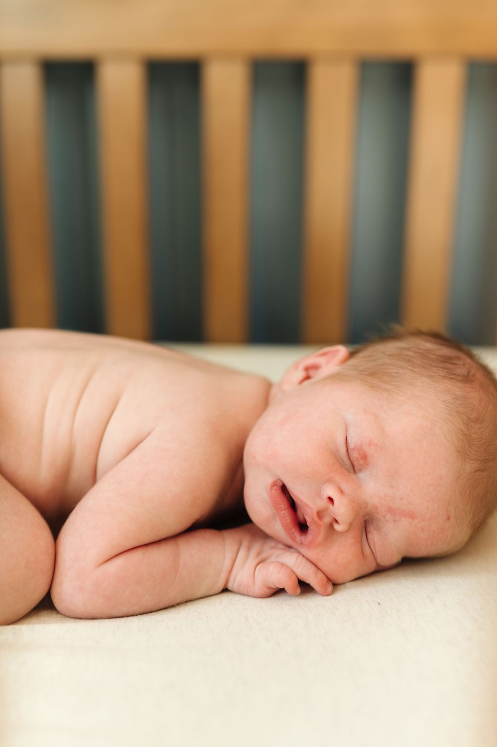 A sleeping newborn baby lying peacefully on white bedding in a wooden crib.
