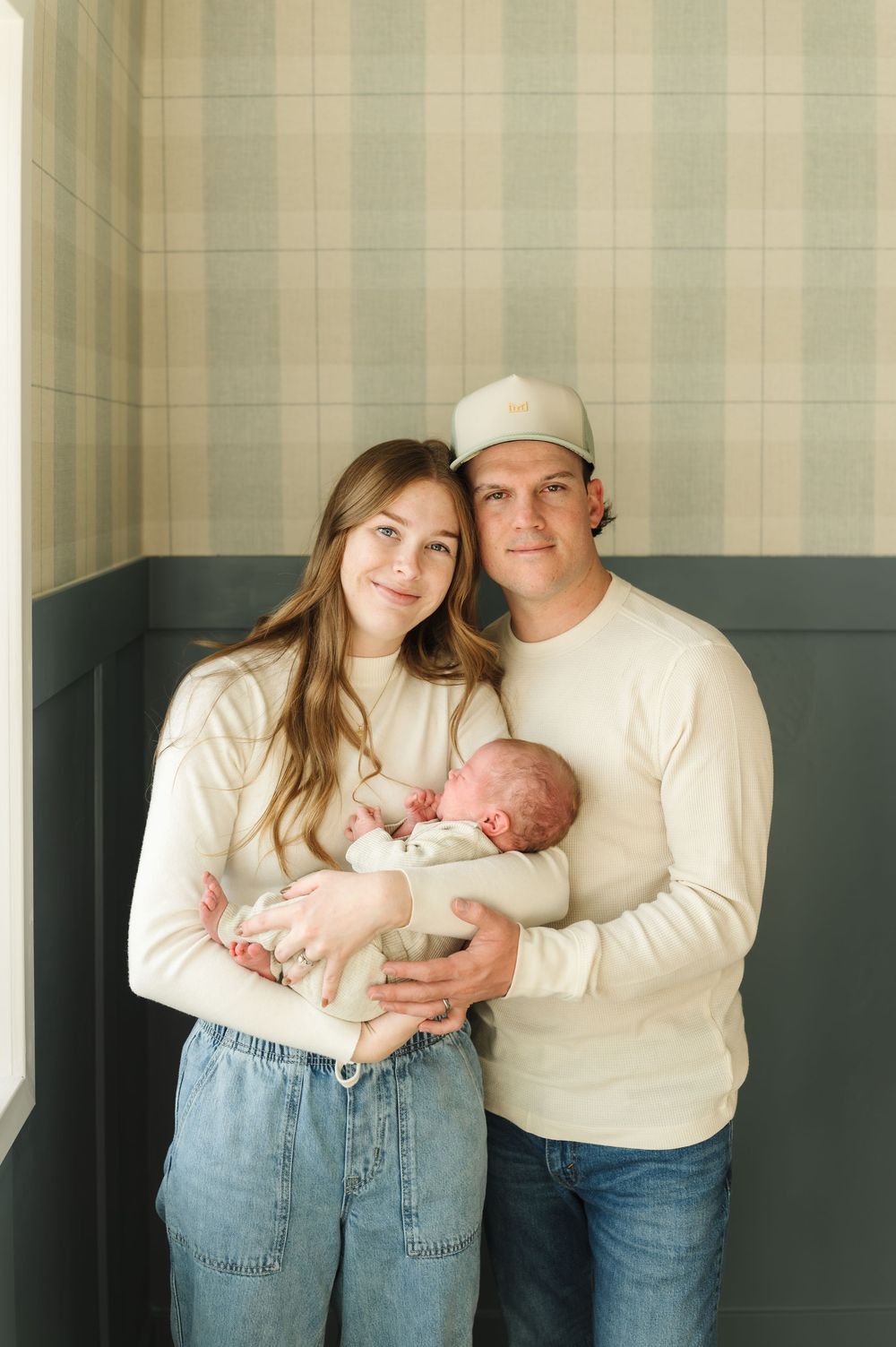 A series of intimate family portraits in matching cream sweaters and jeans with a newborn baby against a neutral wall.