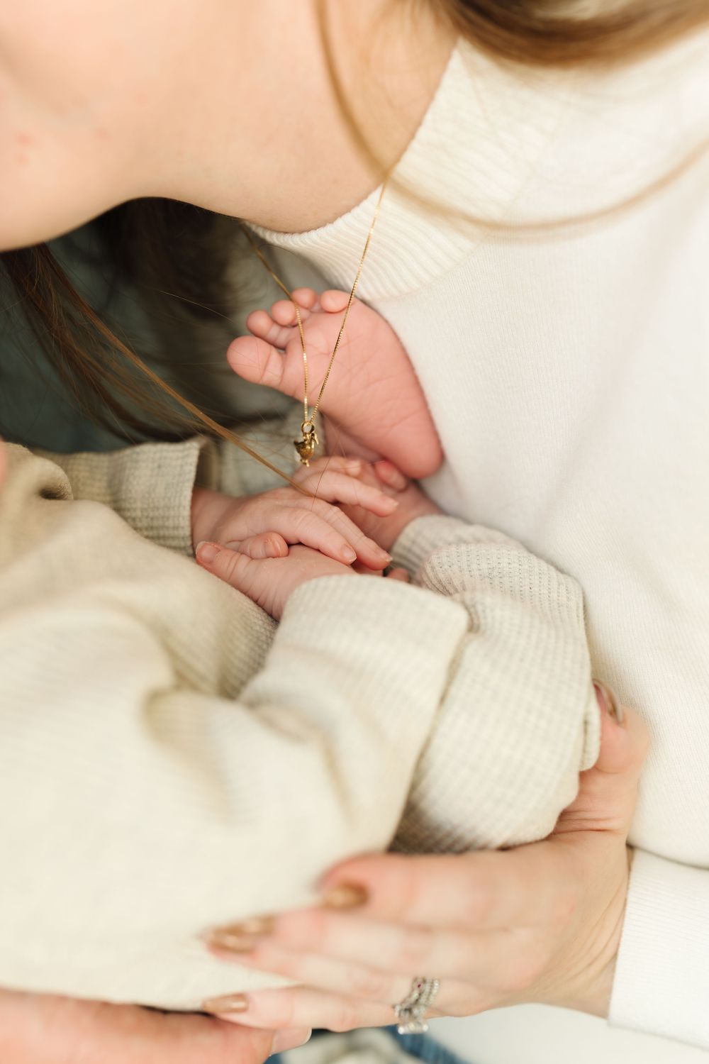 Close-up of hands holding a tiny baby's foot while wearing cozy cream-colored sweaters.