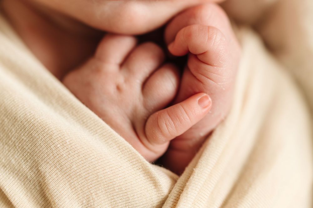 A close-up view of tiny baby feet wrapped in soft beige knit blanket showing delicate toes and skin texture.