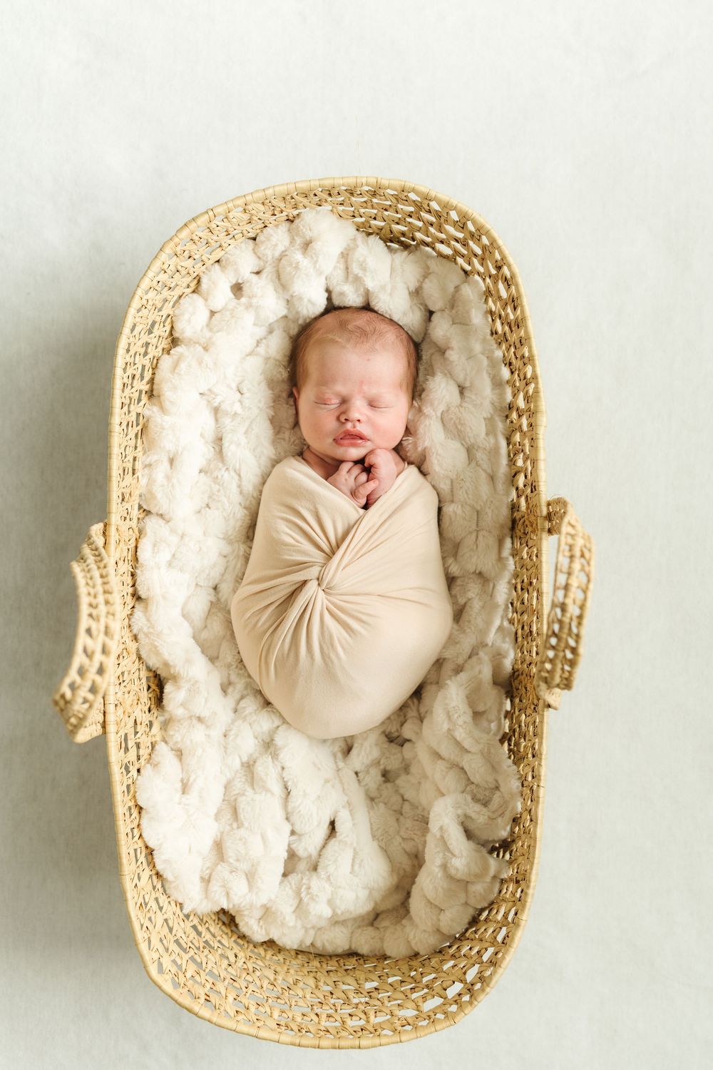 A series of four photos showing a sleeping newborn swaddled in beige fabric nestled in a woven basket with white padding.