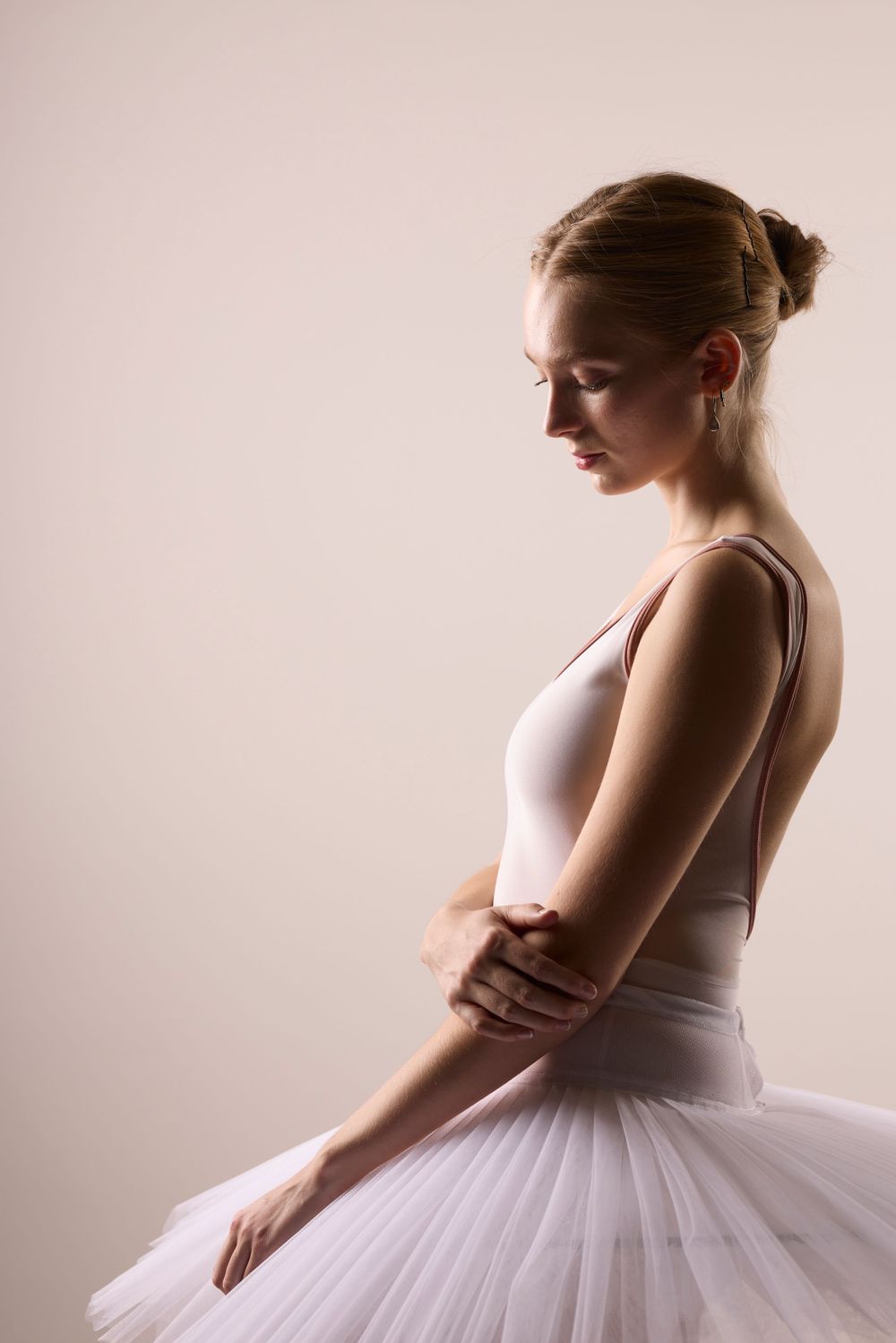 Ballet dancer in white tutu stands in graceful profile against neutral background with elegant posture and form.