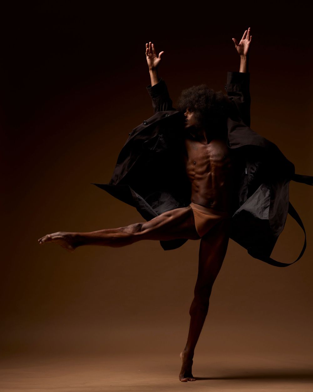 Dramatic dance pose showing silhouetted figure in black coat against dark background.