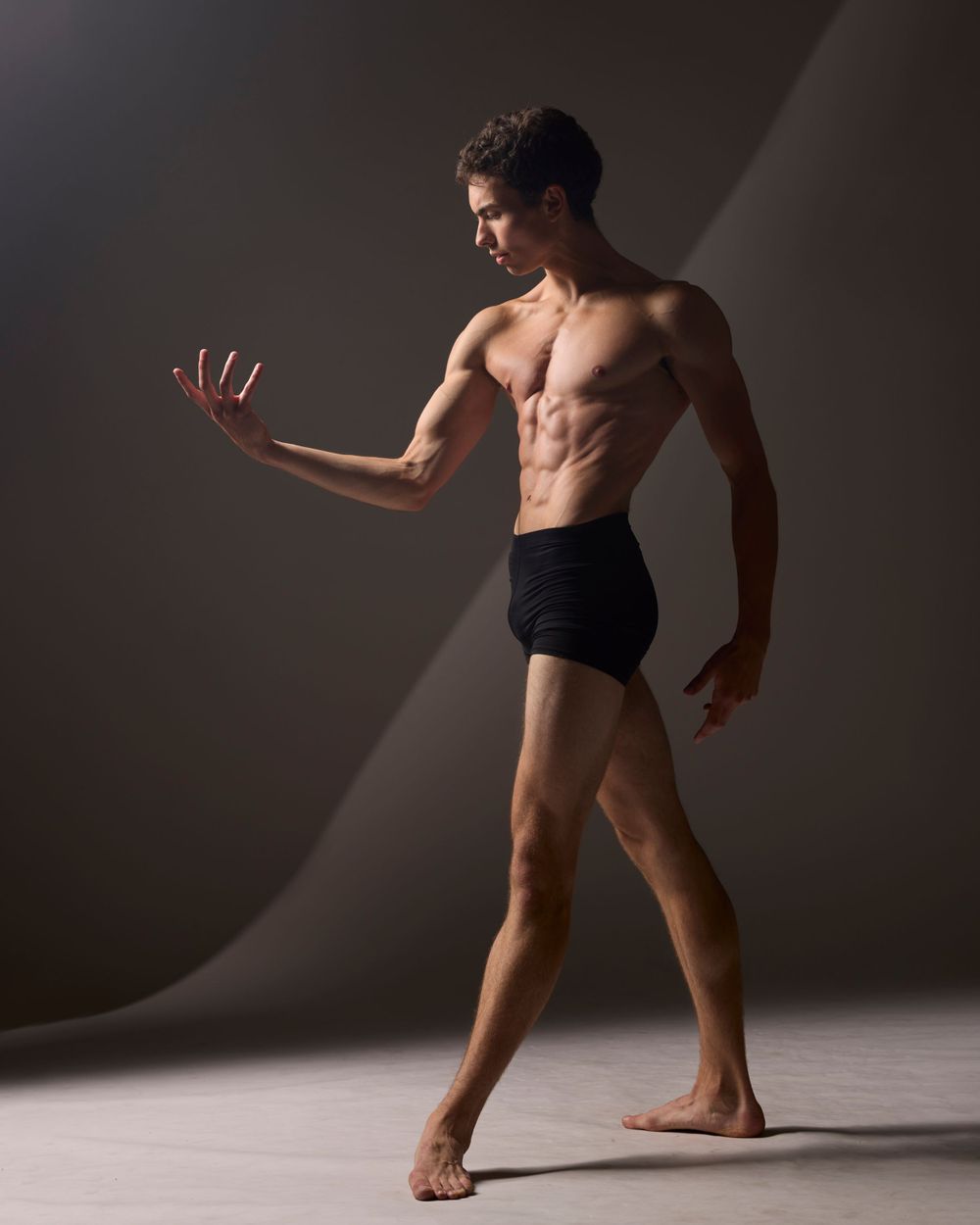 Modern dancer in black shorts demonstrates controlled movement in dramatic lighting.