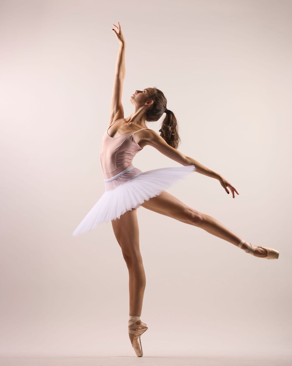 Dancer in white tutu executes perfect ballet pose en pointe with extended arms and leg.